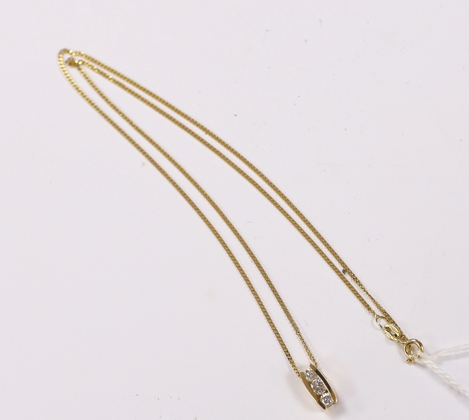 A modern yellow metal and three stone diamond set pendant, 10mm, on a modern 9ct gold fine link chain, 44cm, gross weight 3.1 grams.